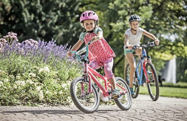 dziewczynka w różowym kubraczku i kaseczku pomyka na rowerku