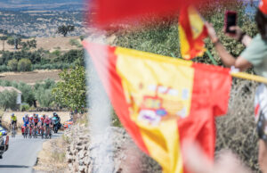 Flaga hiszpańska, w tle przejeżdżający peleton