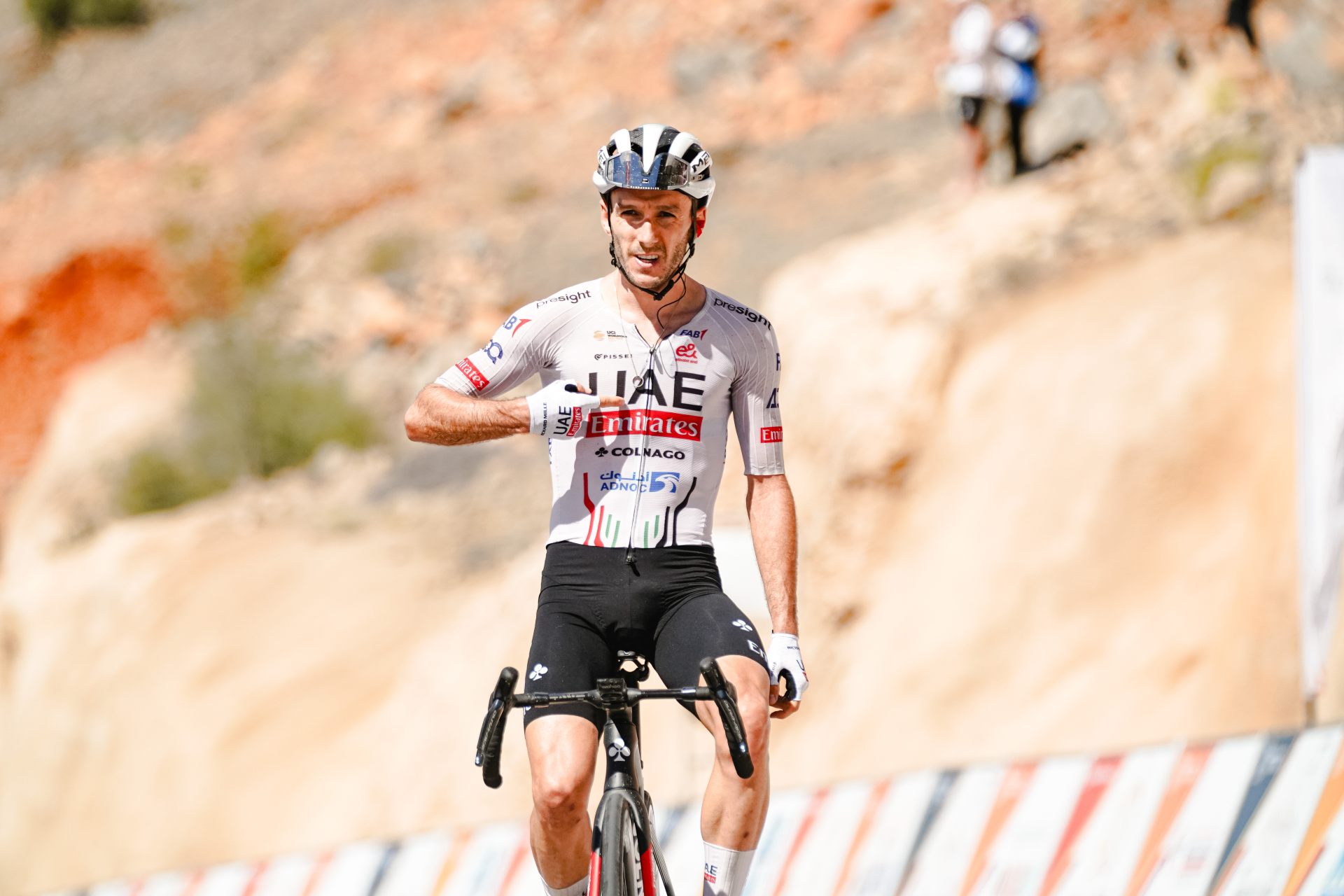 Adam Yates palcem prawej ręki wskazuje na swoją koszulkę podczas finiszu na Zielonej Górze w Omanie