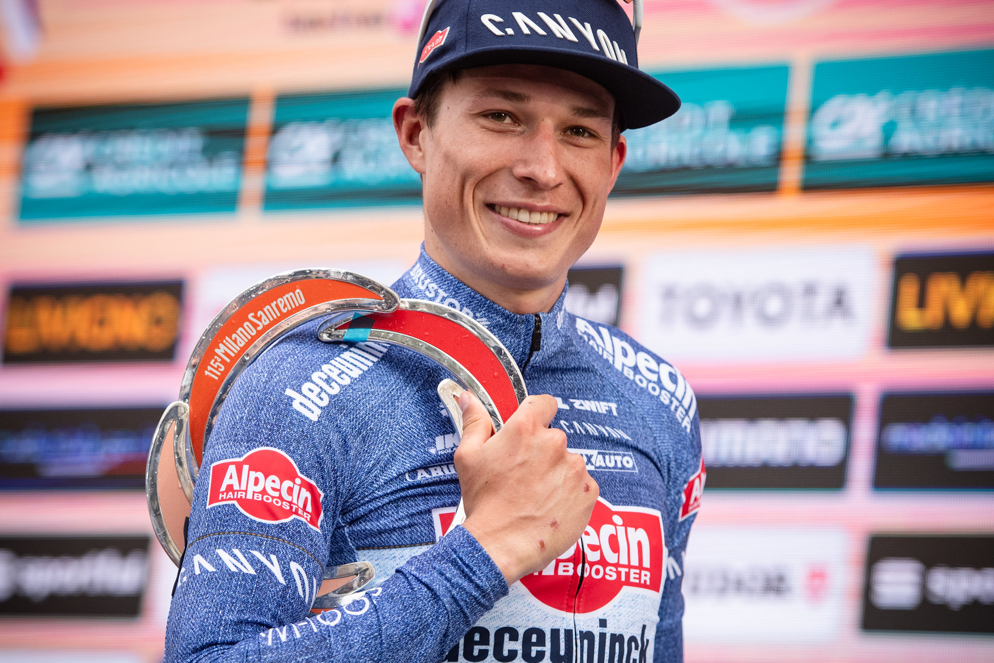 Uśmiechnięty Jasper Philipsen z nagrodą za zwycięstwo w Mediolan-San Remo na ramieniu